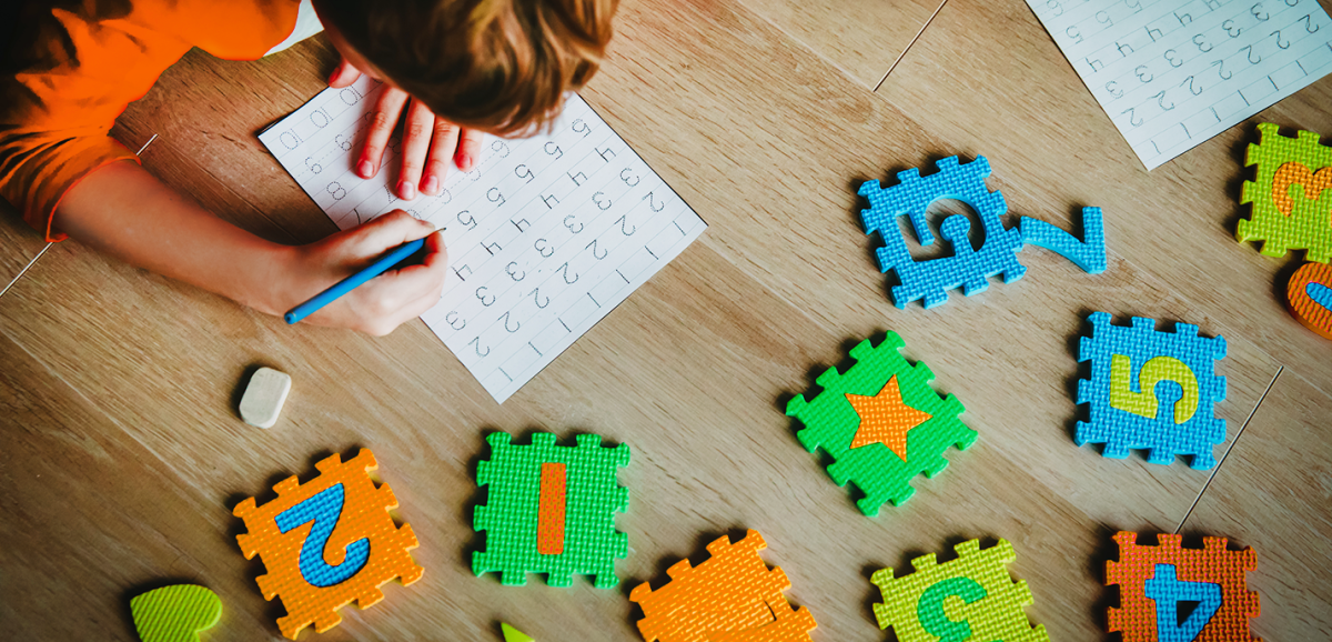 A child plays with foam blocks and practices numbers on the floor at home.